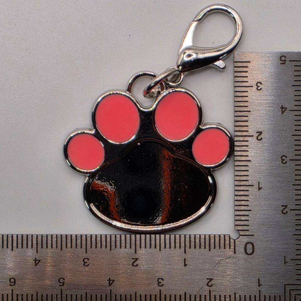 Paw print keychain with pink circles next to a ruler for scale on a gray background