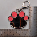 Paw print keychain with pink circles next to a ruler for scale on a gray background
