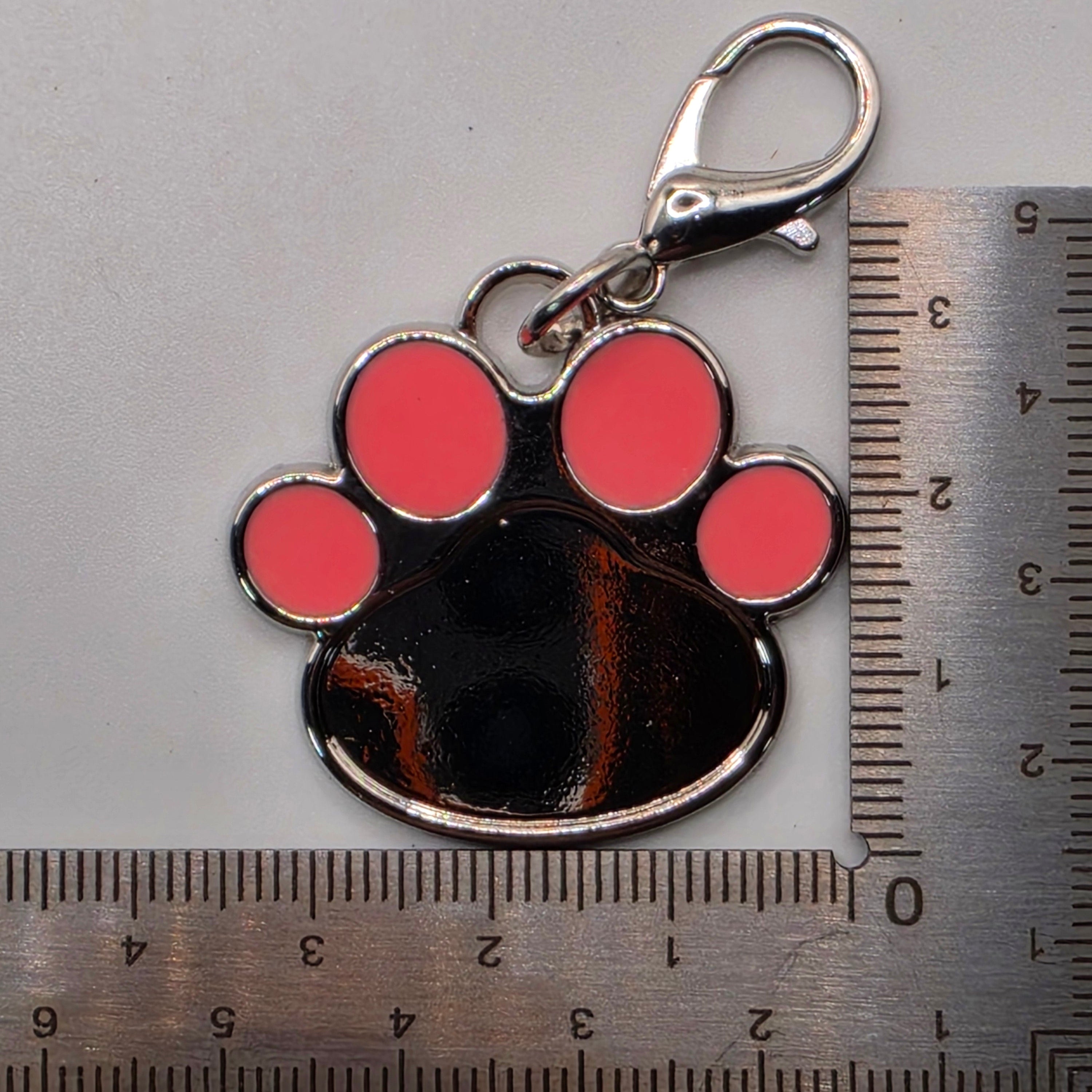 Paw print keychain with pink circles next to a ruler for scale on a gray background