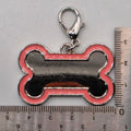 Dog bone-shaped keychain with a clasp next to a ruler for scale on a gray background