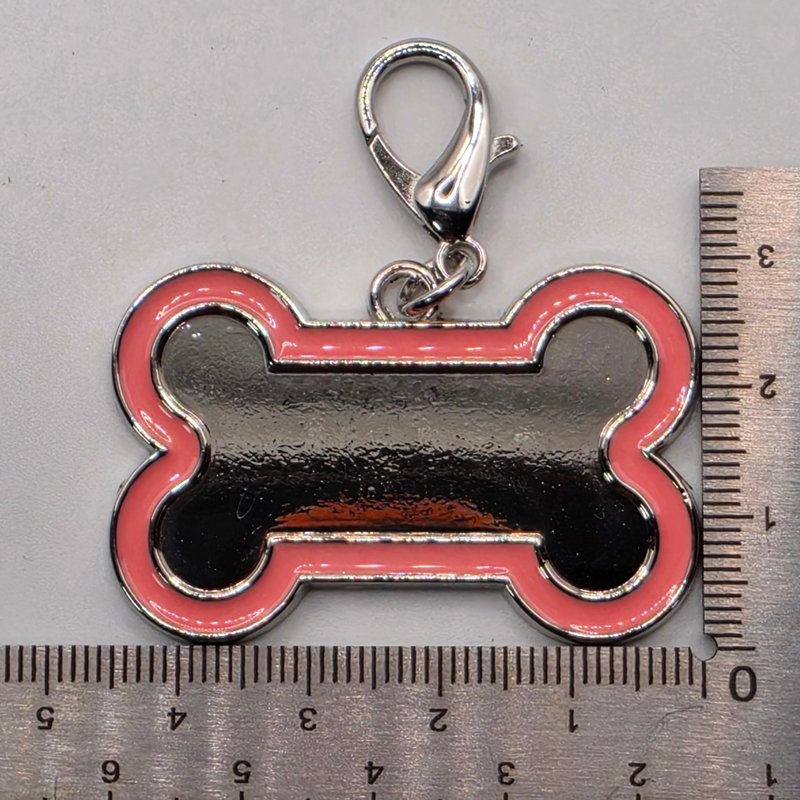 Dog bone-shaped keychain with a clasp next to a ruler for scale on a gray background