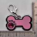 Pink bone-shaped keychain with a silver clasp and red gemstone, measured against a ruler on a gray background.