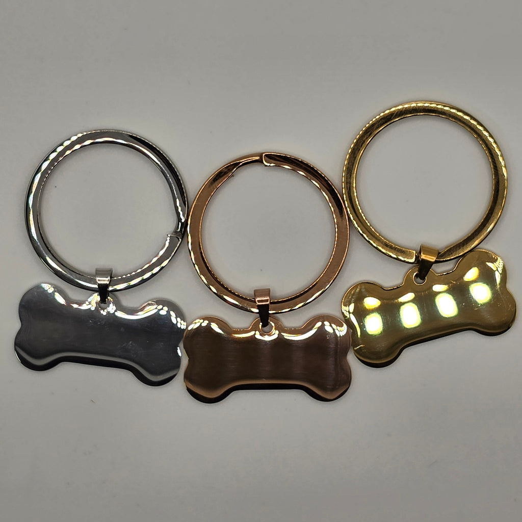 Three keychains shaped like a paw, a dog collar, and a bone on a gray background.