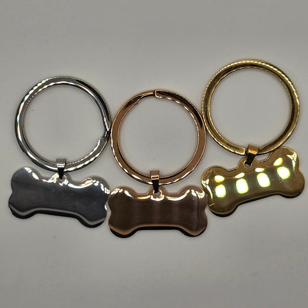 Three keychains shaped like a paw, a dog collar, and a bone on a gray background.