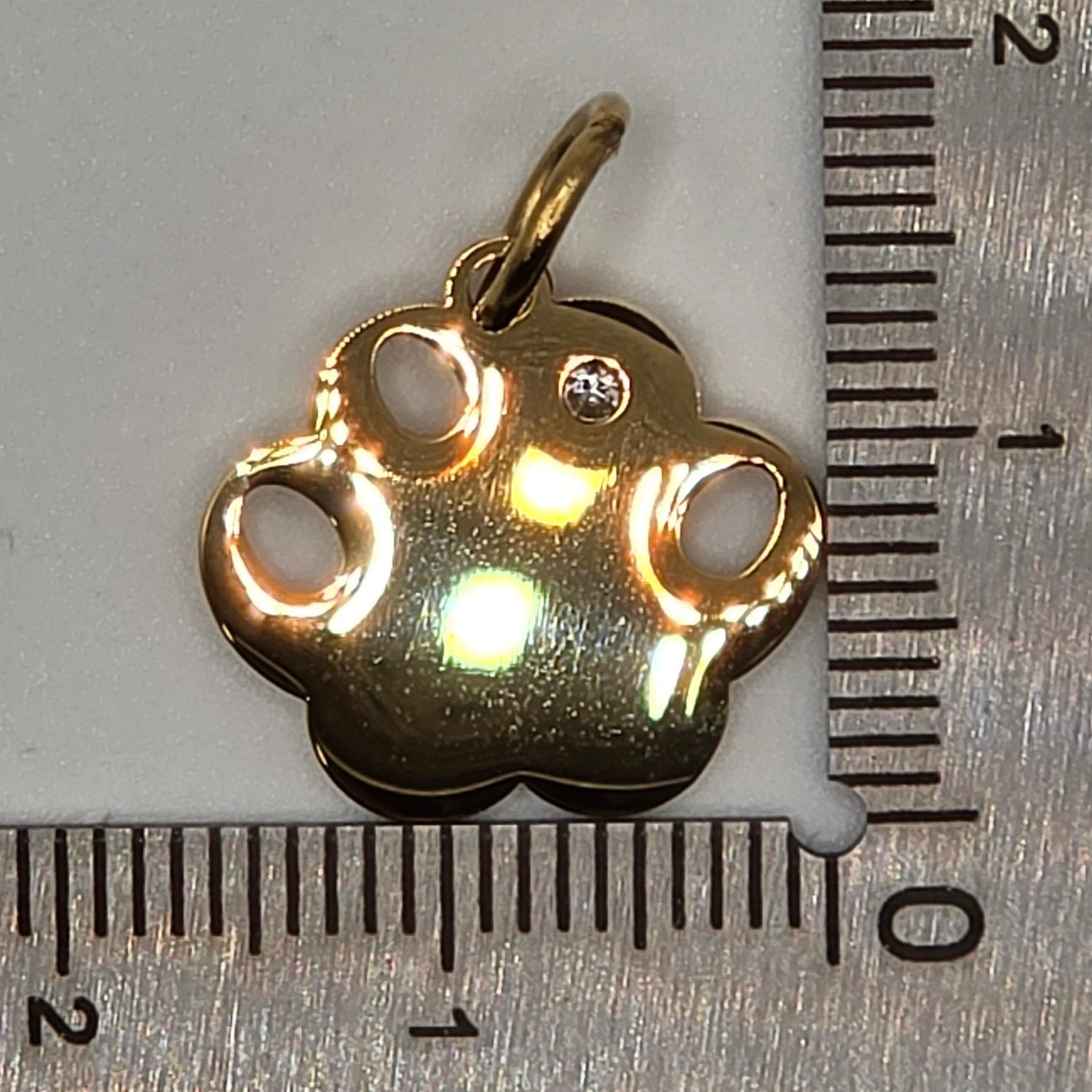 Gold charm next to a ruler on a white background