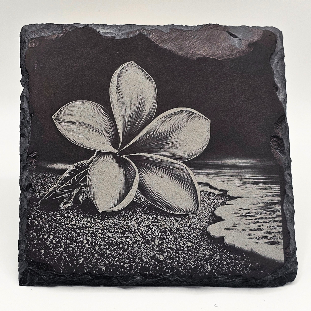 Slate tile with a black and white frangipani flower design on a beach background