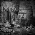 Pair of cowboy boots next to a barrel and glass in a rustic setting