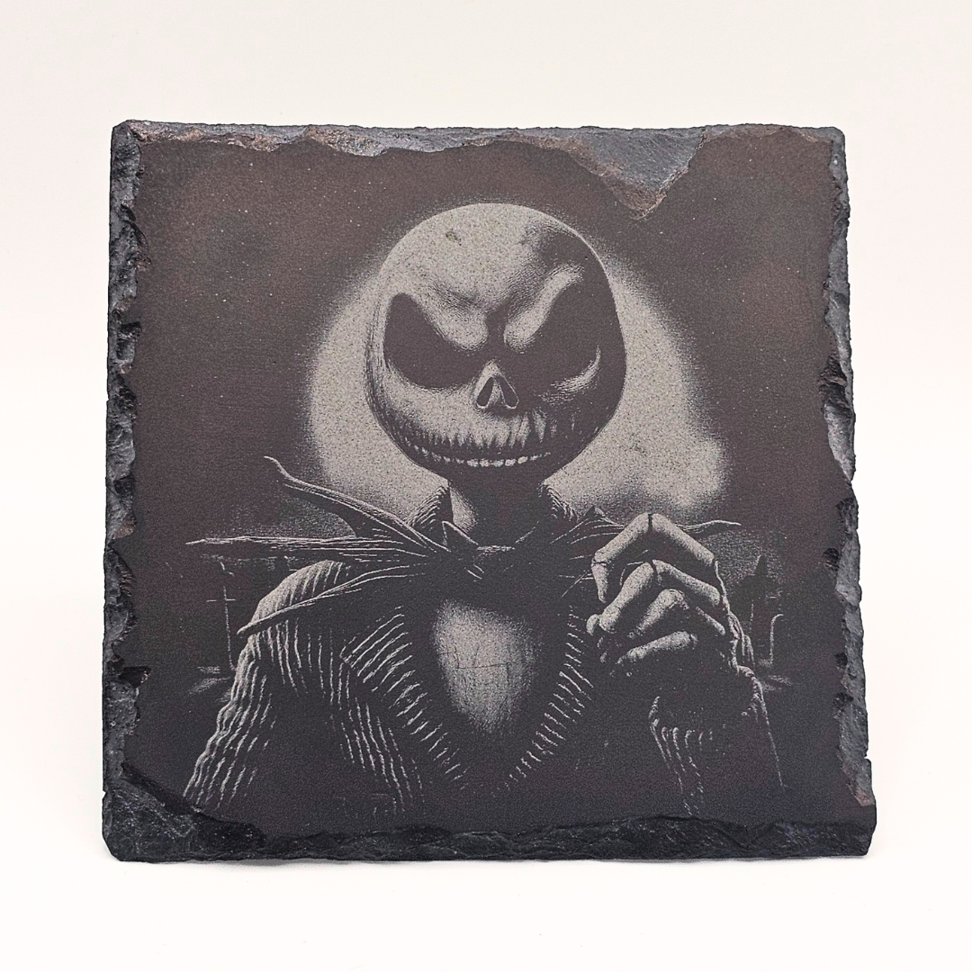 Slate coaster with a black and white illustration of a character with a wide smile on a dark background.