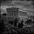 Black and white image of a classical temple on a rocky outcrop with a dramatic sky.