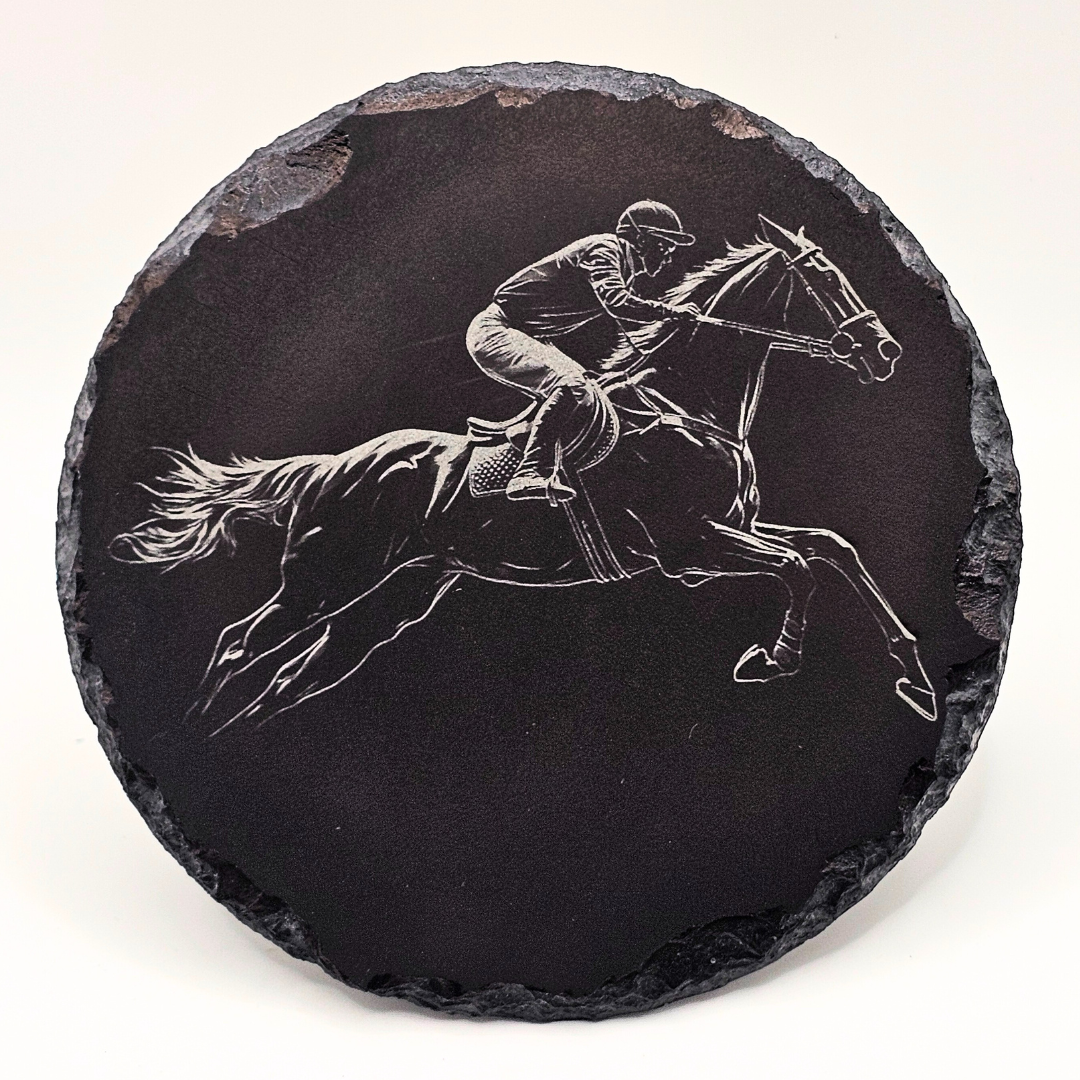 Round black slate coaster with engraved image of a horse and rider on a white background