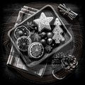 Decorative tray with star and tree-shaped cookies, dried citrus slices, and pine cones on a wooden surface.