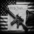 Rifle with scope on a document titled 'We the People' on an American flag