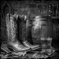Pair of cowboy boots with a wooden barrel and glass in a rustic setting