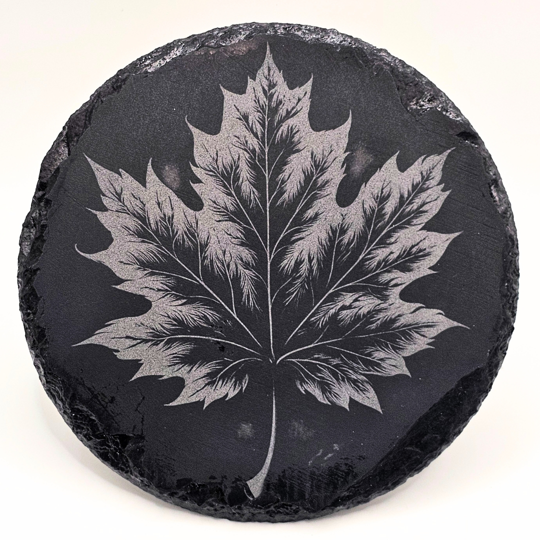 Round black stone coaster with a silver maple leaf engraving on a white background