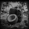 Tiki mug made from a coconut with a flower on a beach setting