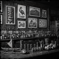 Bar with various bottles, decorative items, and framed artwork on a wooden wall.