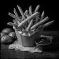 Black and white photo of a paper container filled with French fries on a wooden surface.