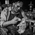 Person in a horror-themed costume feeding a puppy with a bottle, sitting on a wooden bench.