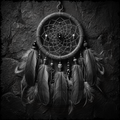 Black and white dreamcatcher with feathers and beads on a dark stone background