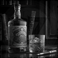 Bottle of John Stevens whiskey with a glass of ice on a wooden surface.