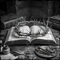 Crown of thorns on an open book with a quill and ink bottle on a wooden surface.