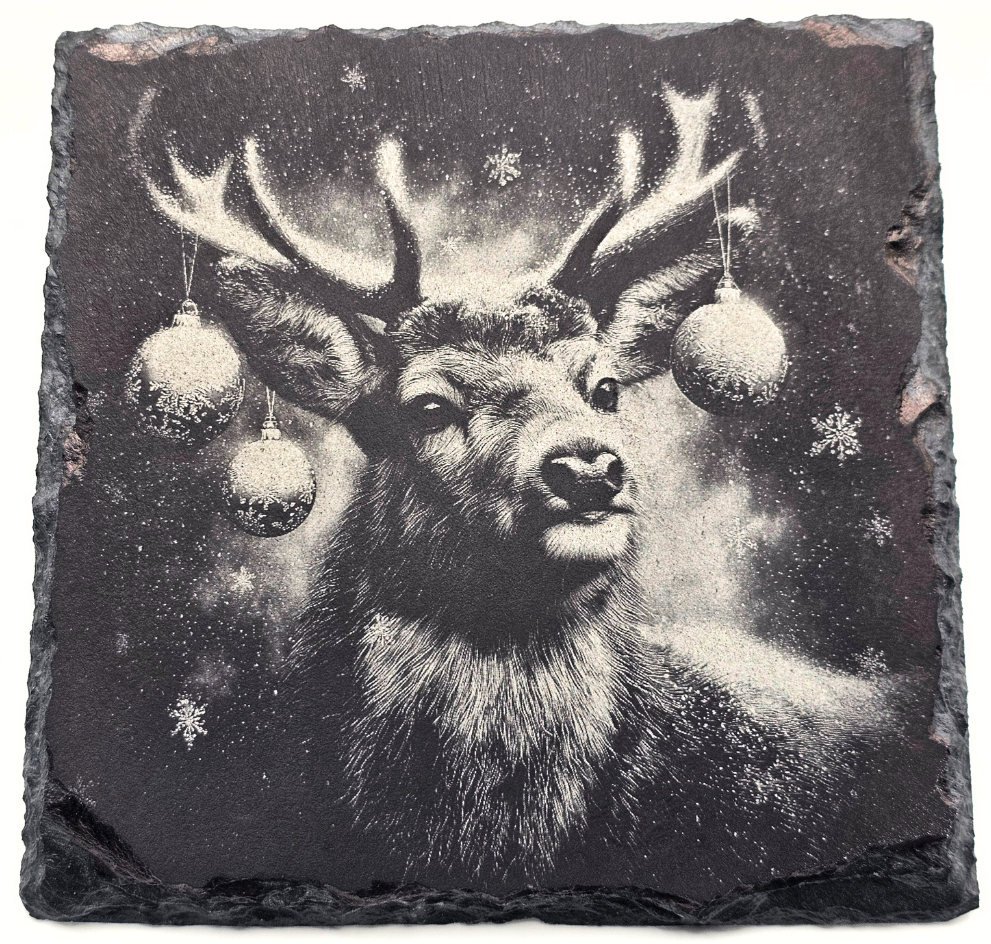 Decorative slate with a black and white illustration of a deer's head surrounded by Christmas ornaments and snowflakes.