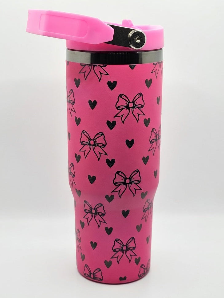 Pink tumbler with black heart and bow pattern on a white background