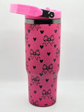 Pink tumbler with black heart and bow pattern on a white background